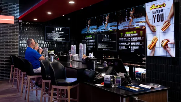 A photo of people sitting at a bar watching a UFC fight on TVs behind the bar. A sign near the left side of the picture says "Rutter's. Made for you."