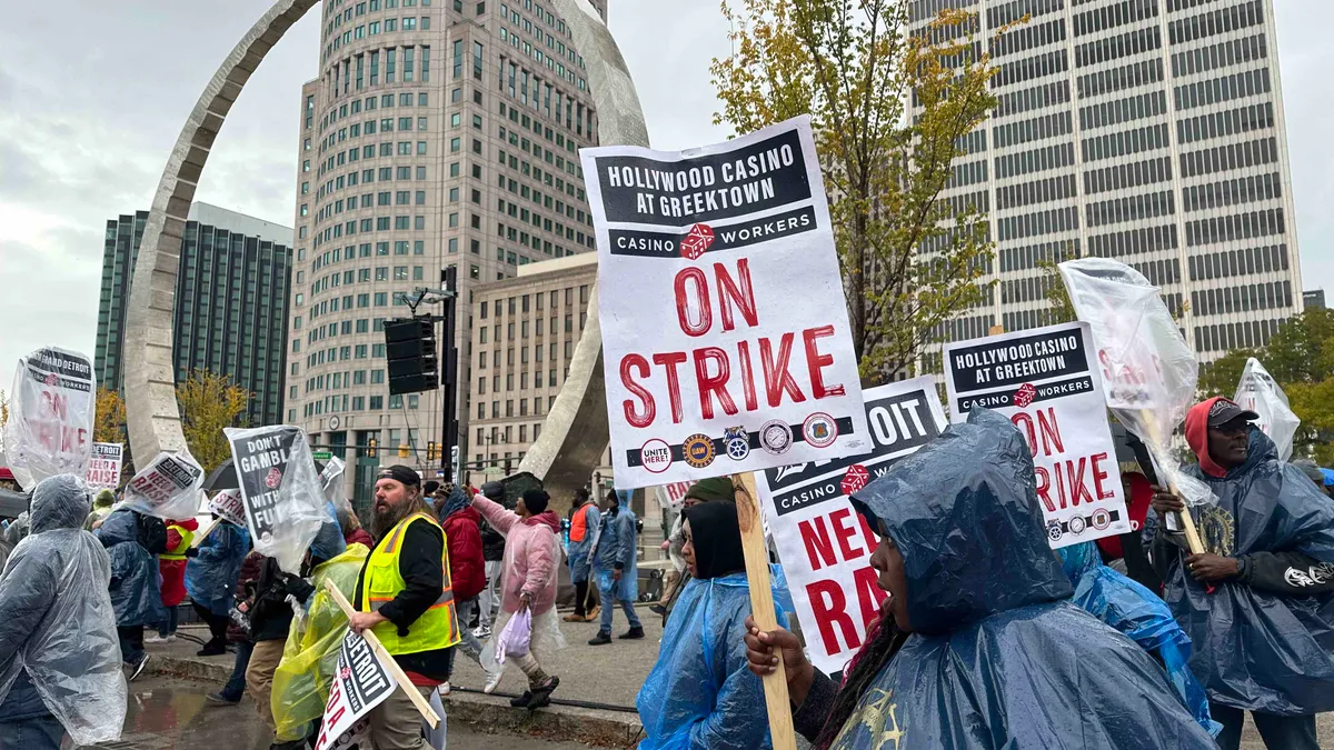 Workers in ponchos and rain gear hold picket signs that read "ON STRIKE."