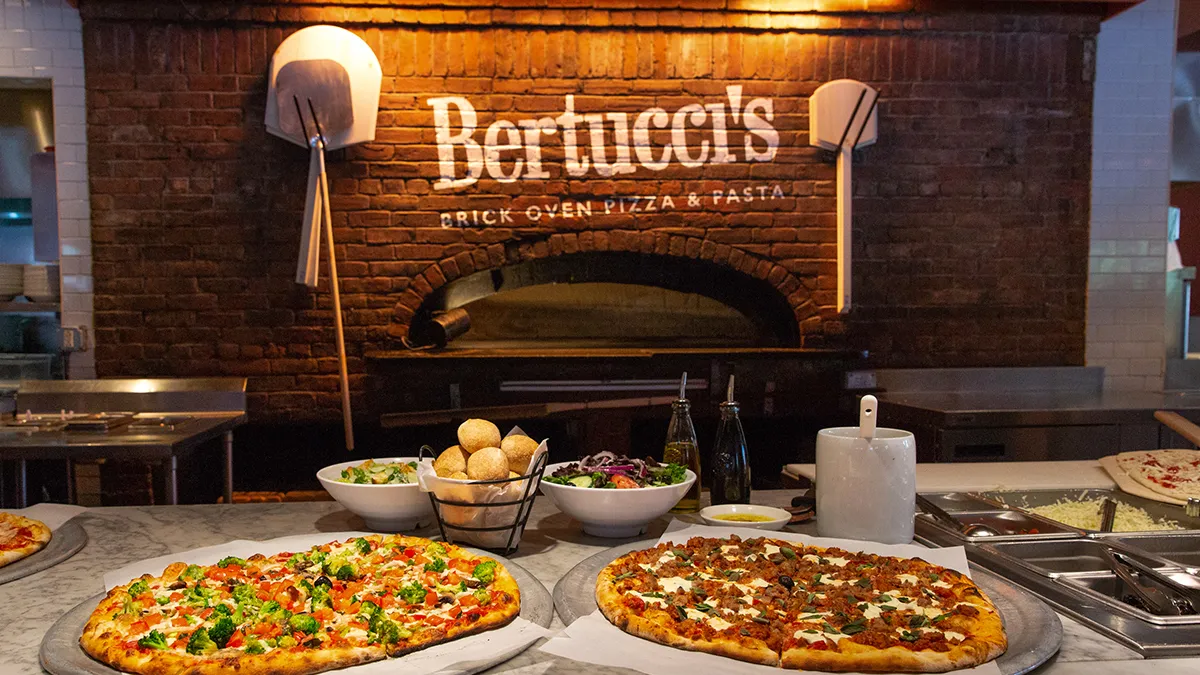 An image of two pizzas in front of a pizza oven.