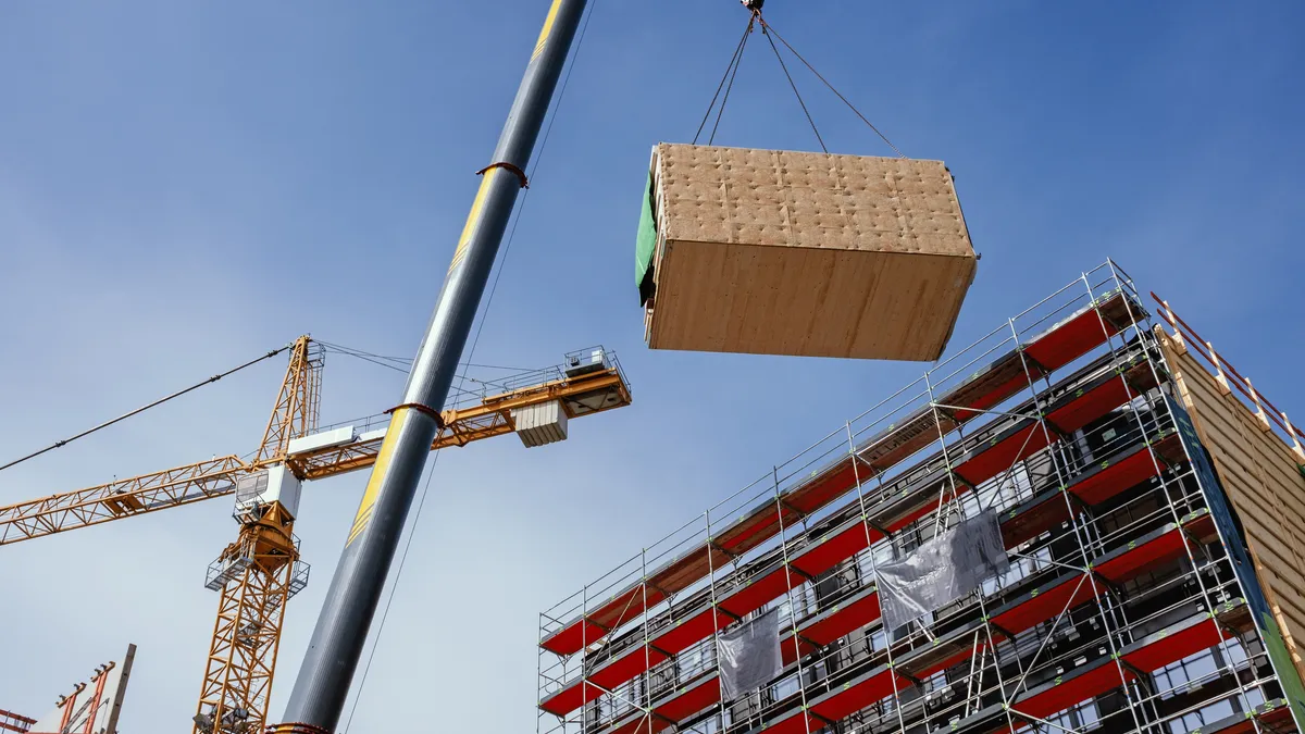 A crane hoists a built piece of a building into place.