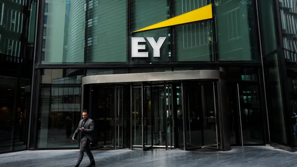 The photo shows a business person exiting an office building's door over which an Ernst & Young label is hung.