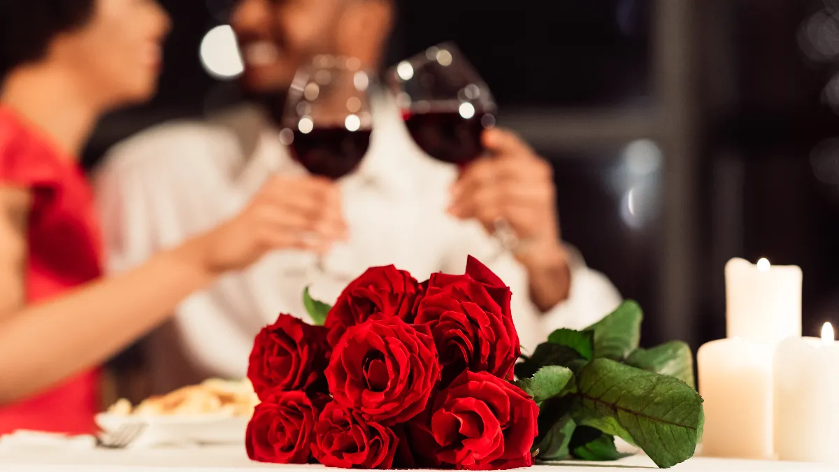 An image of two people with wine and a bouquet of roses in the foreground.