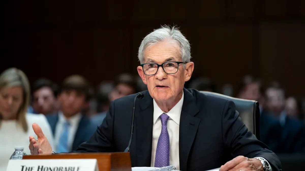 Federal Reserve Chair Jerome Powell, wearing a suit and tie, addresses senators with a microphone in front of him and people behind him.