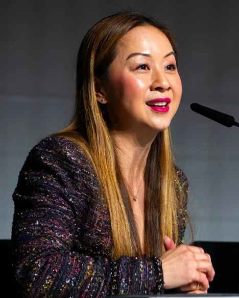 A person speaks on a microphone while another person sits next to them.