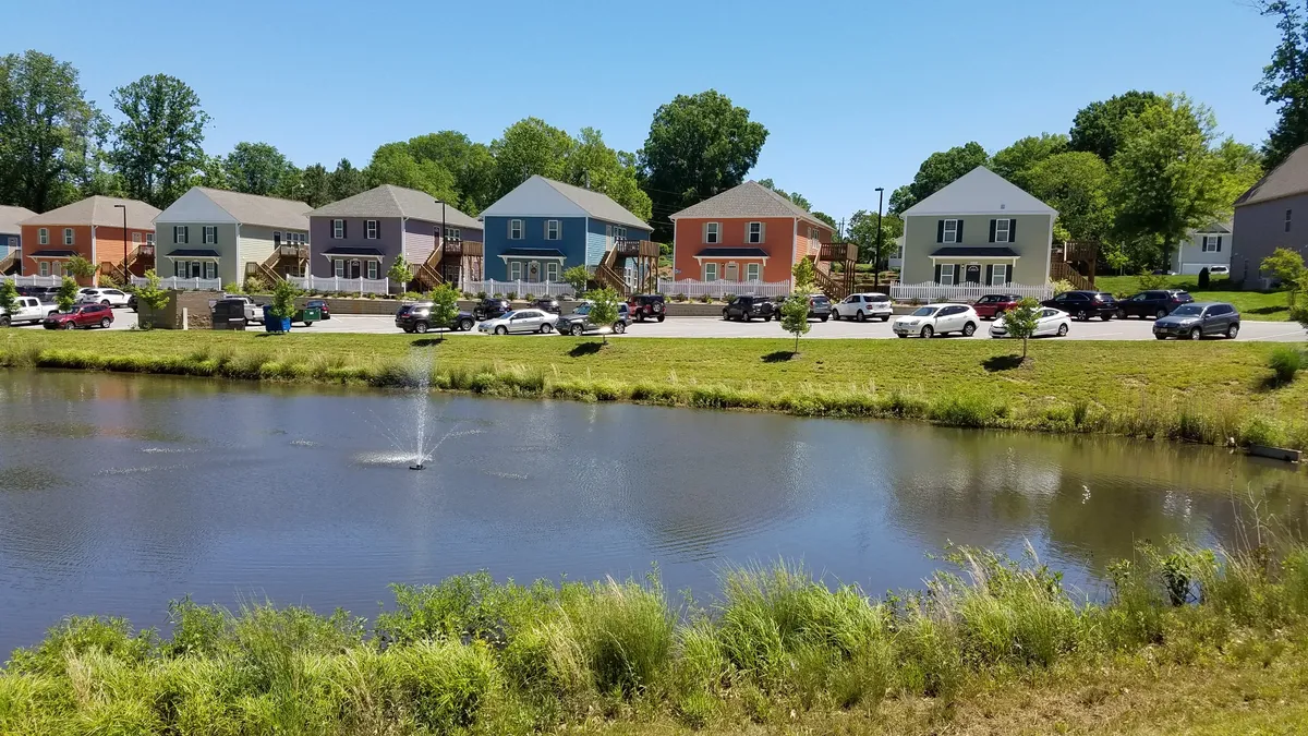 Detached homes with a parking lots, cars and a pond in the foreground