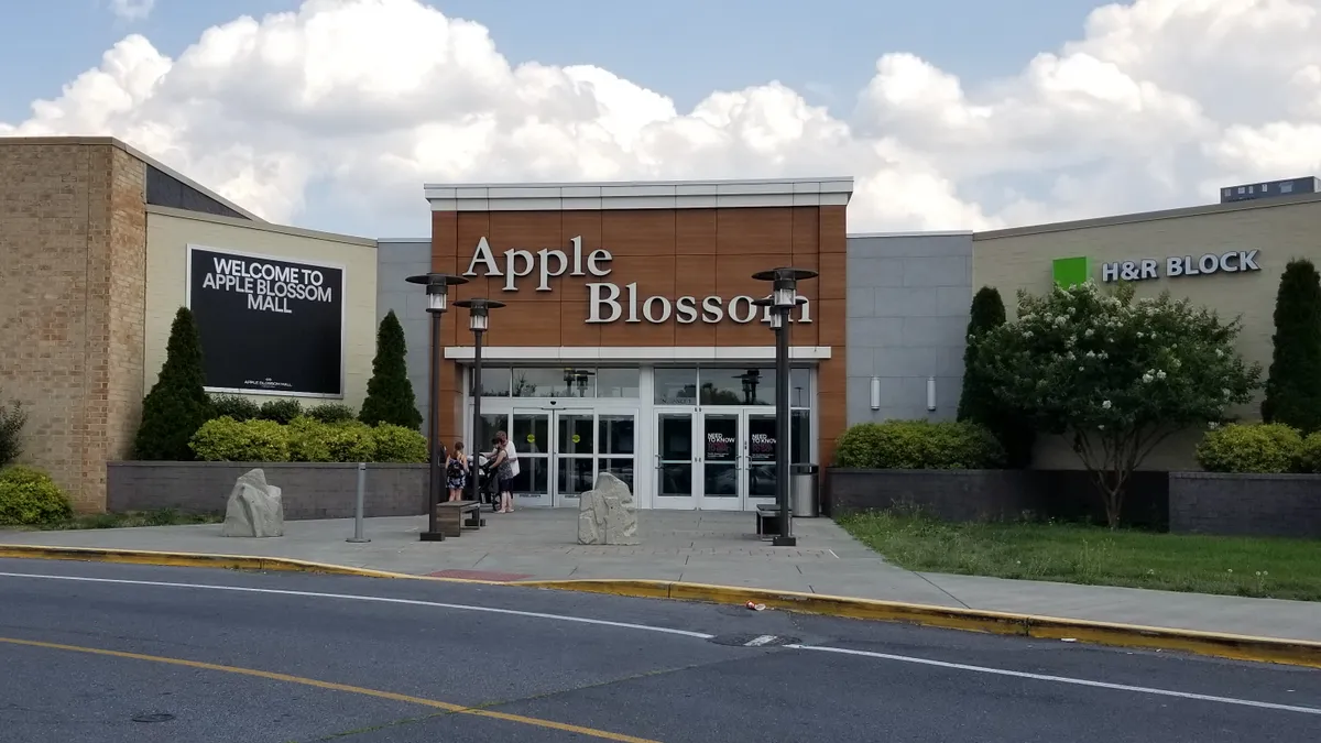 Main entrance to a shopping center, under puffy clouds against a pale blue sky.