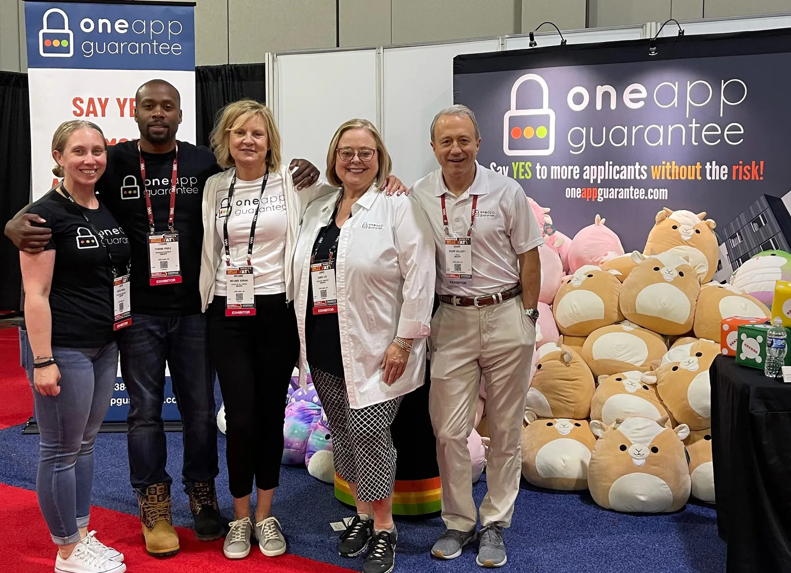 Four people stand together at a booth in front of a pile of plushes.