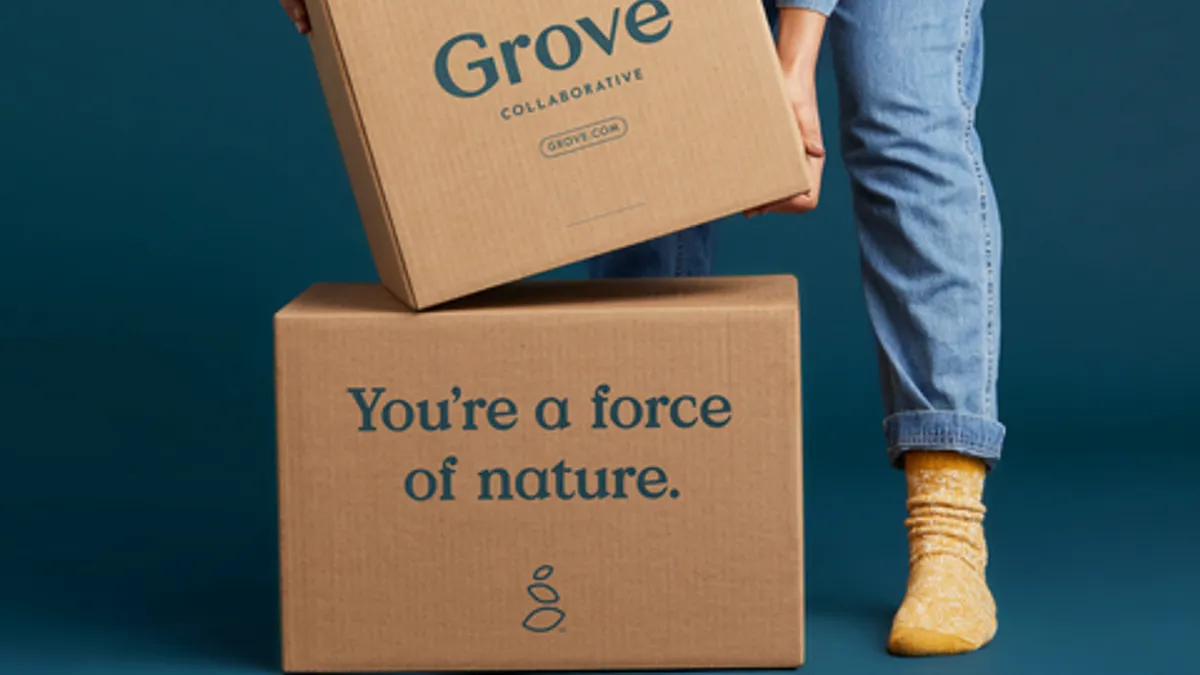 A person wearing blue jeans and yellow socks deals with two big cardboard boxes with green lettering.