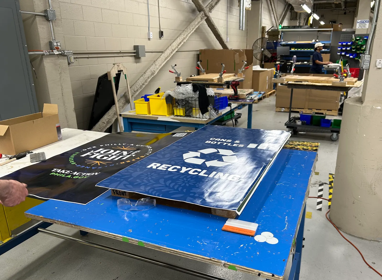 Two signs lay on a table, advertising a logo for Philadelphia and another that says "Cans & Bottles Recycling"