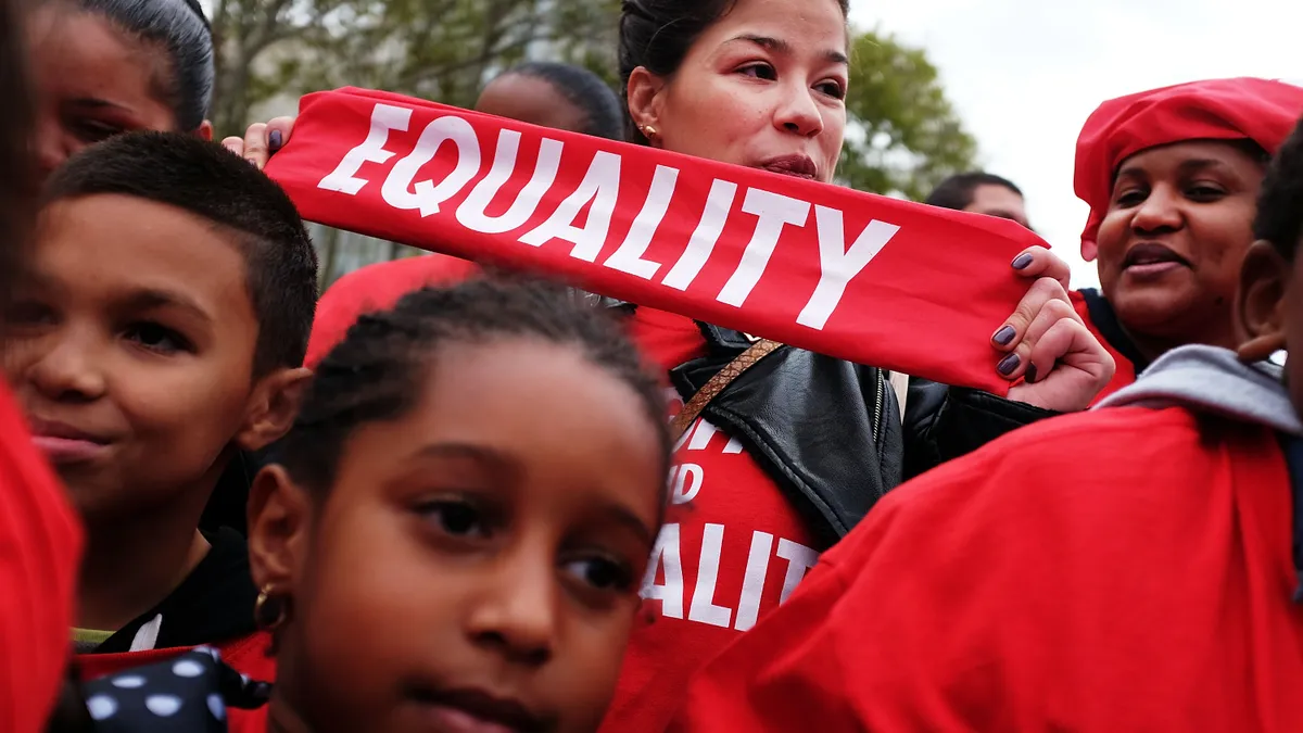 A protester in a crowded rally of students, parents and educators holds a red sign that says "Equality".