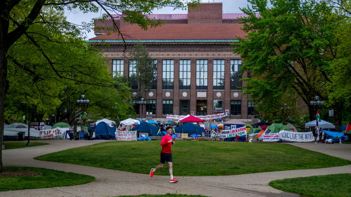 A person runs on the sidewalk past a protest encampment on the campus of the University of Michigan.