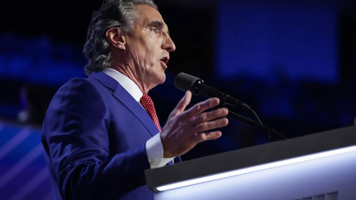 A man in a blue suit speaks at a podium.