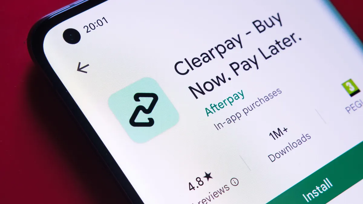 A "Clearpay - Buy Now. Pay Later." app is seen on a phone lying on top of a red surface. 