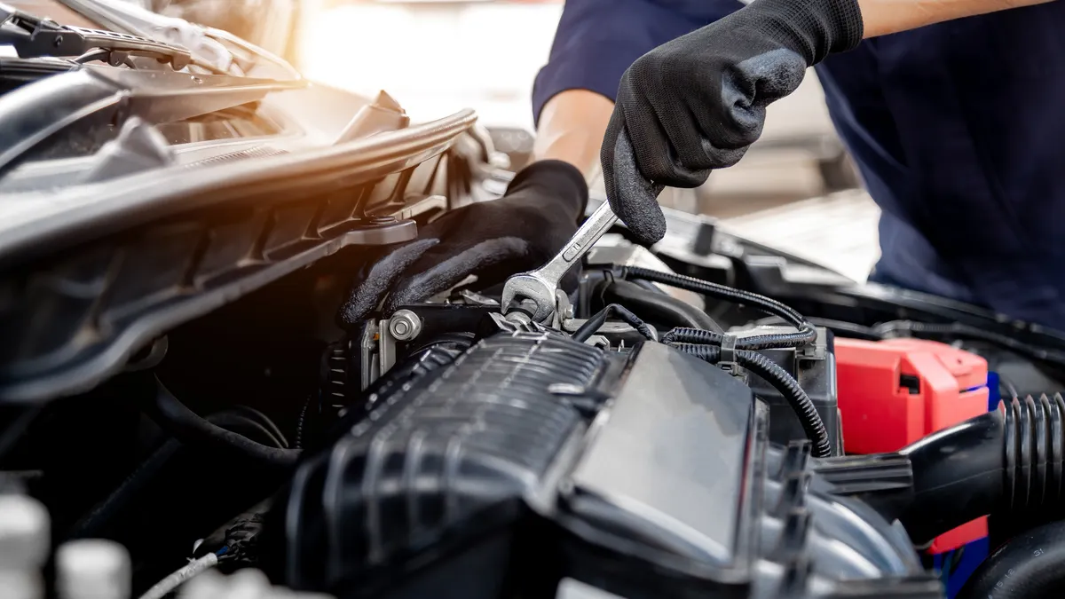 A person holding a wrench works on a car engine.