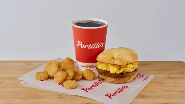 An image of a breakfast sandwich, coffee and hashbrowns on a table