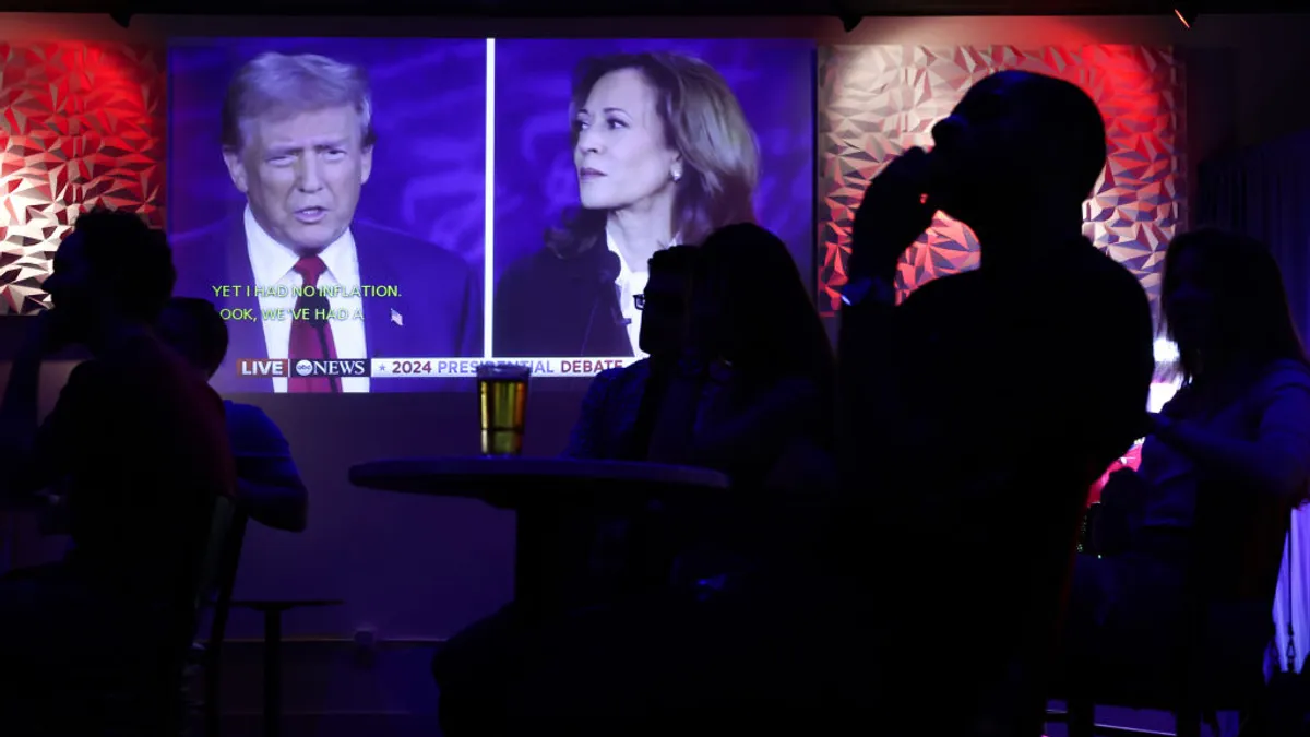 People in a bar watch a TV screen with former President Donald Trump and Vice President Kamala Harrris debating.