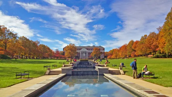 Classical brick building with white columns framed by trees with grass and a reflecting pool in the foreground.