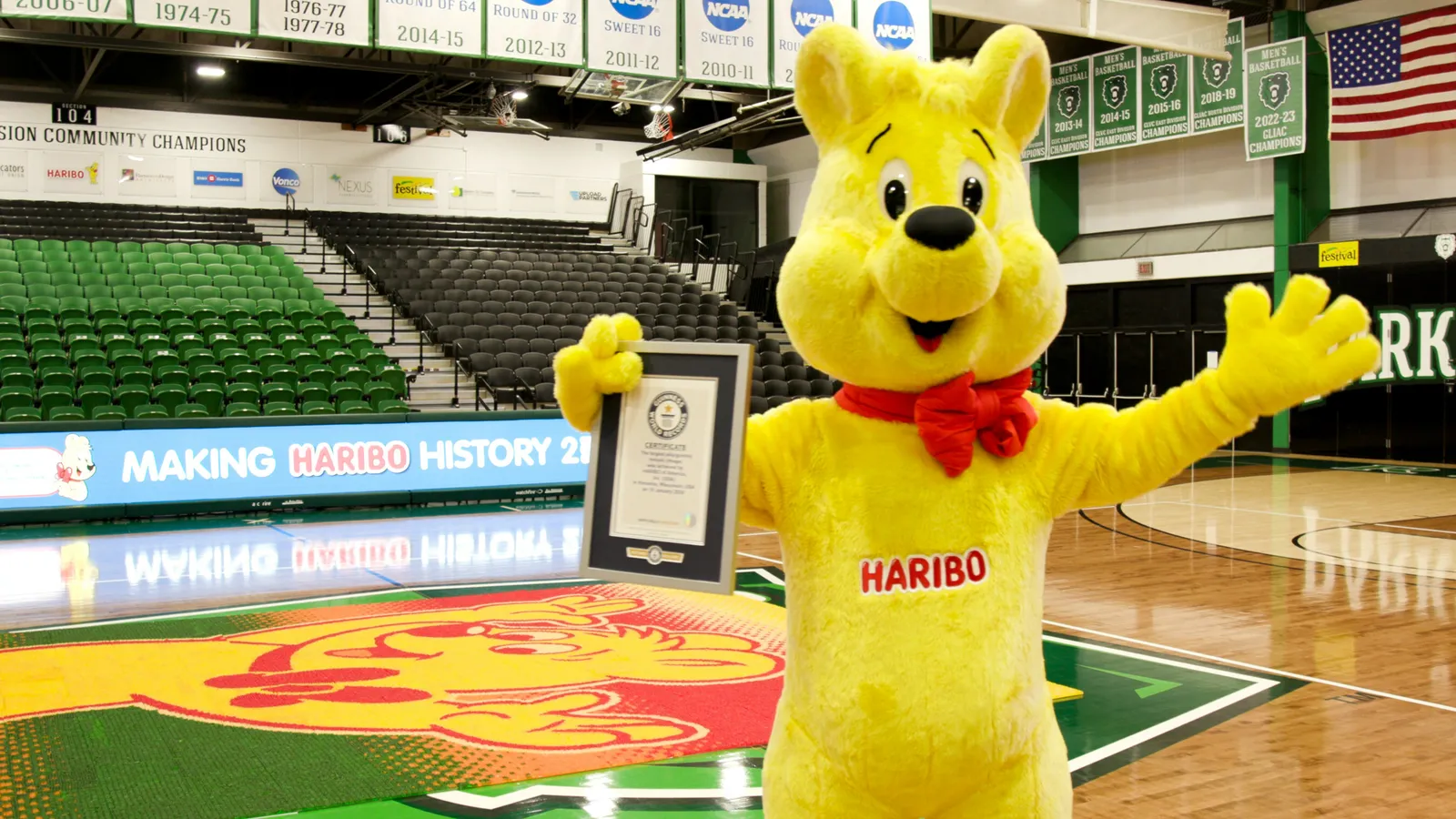 A yellow Haribo bear mascot holds a plaque in front of a gummy mural.