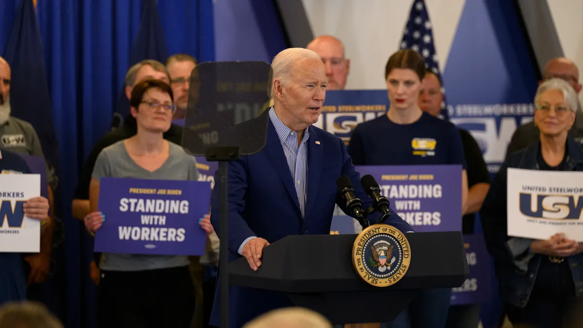 A man stands at a podium in front of people holding bright signs.