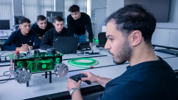A group of young men work around a laptop and controller rig.