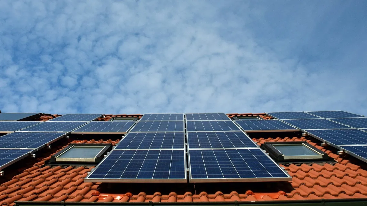 Solar panels laid out on a red shingle rooftop with a blue sky in the background.