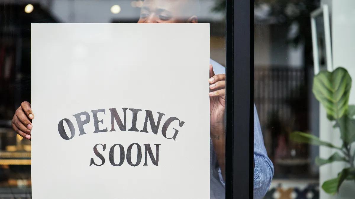 An image of a man setting up an opening soon sign.