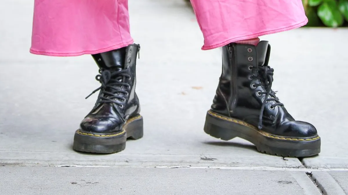 A closeup of a person's outfit holding a black Gucci bag and wearing Dr. Martens boots.