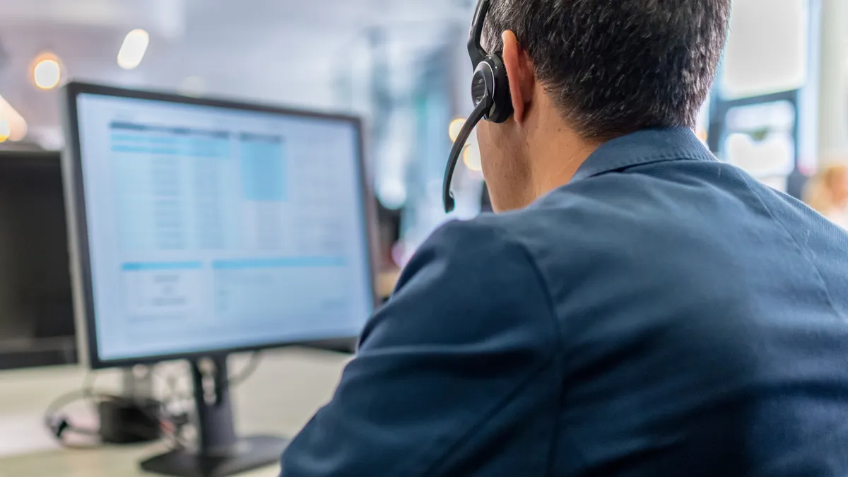 Close-up of customer service representative wearing wireless headset working on desktop computer in call center.