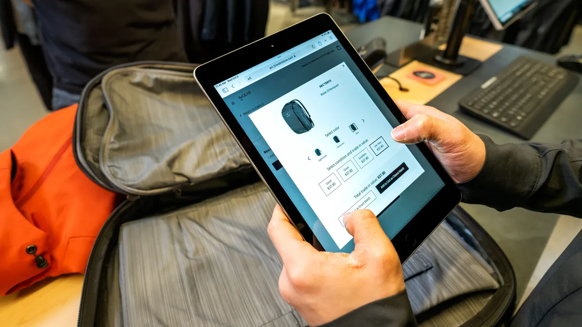 A person holds a tablet and looks at clothing.