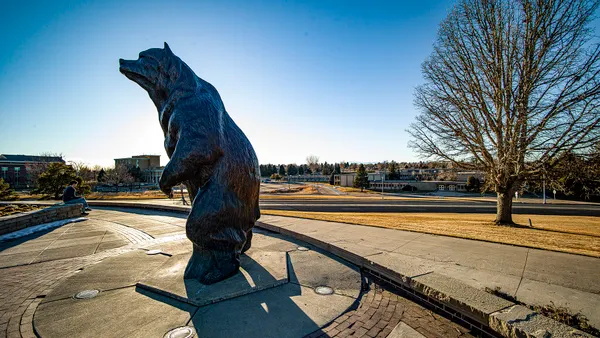 Statue of bear mascot with student sitting nearby.