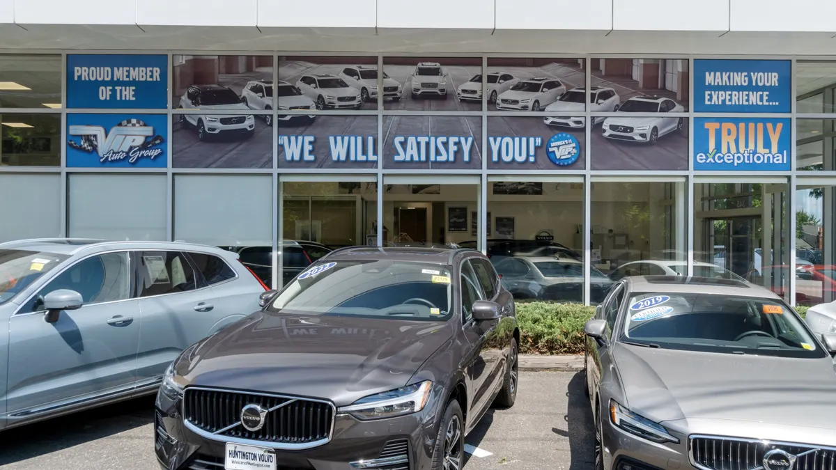 Three vehicles sit in front of a dealership, with signs that say "Proud Member of the VIP Auto Group," "We Will Satisfy You!" and "Making Your Experience... Truly Exceptional! plastered on the windows.
