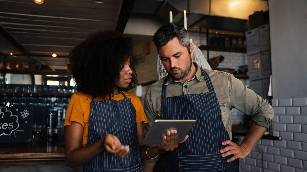 A man and woman discussing wearing aprons in a restaurant