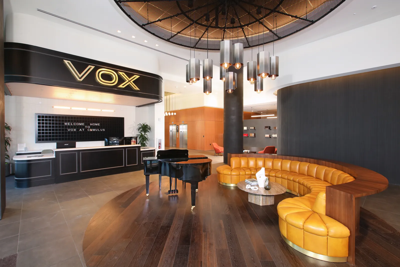 A large room with a winding couch and a grand piano, plus the word "VOX" on a sign over a reception desk.