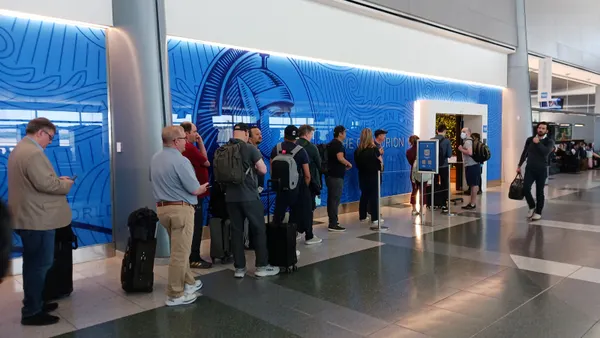 People wait in a line outside an entrance flanked by glass with the American Express logo.