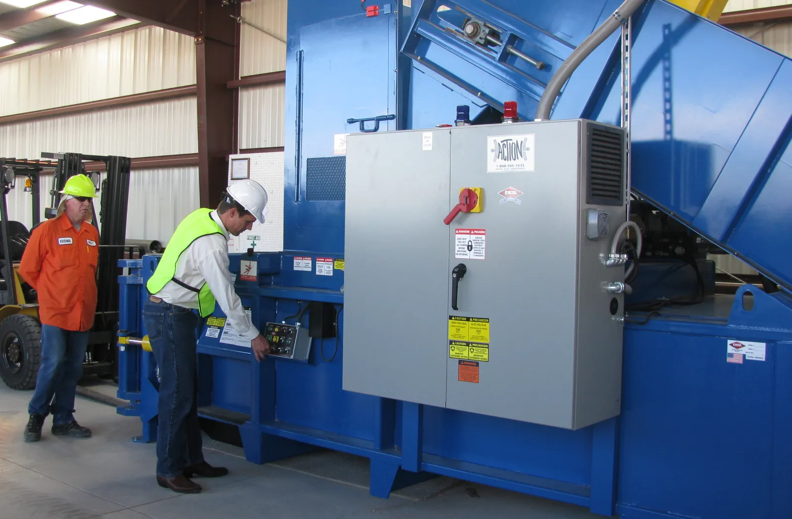 Two people in safety gear inspect a cardboard baler in New Mexico