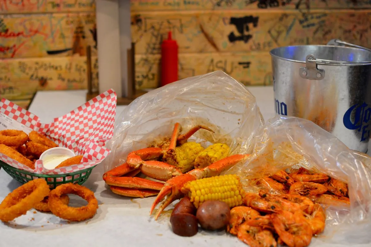 A table with onion rings and crab legs, corn and shrimp in plastic bags.