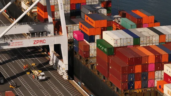 In an aerial view of a shipping container is loaded onto a truck on a dock at an ocean port in California.