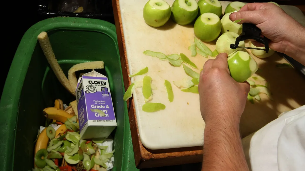 Person peeling food next to compost bin