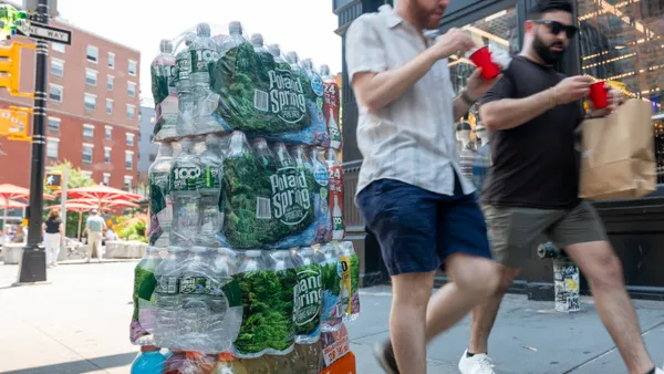 Cases of Poland Spring bottled water sit stacked on a city sidewalk as people walk past.