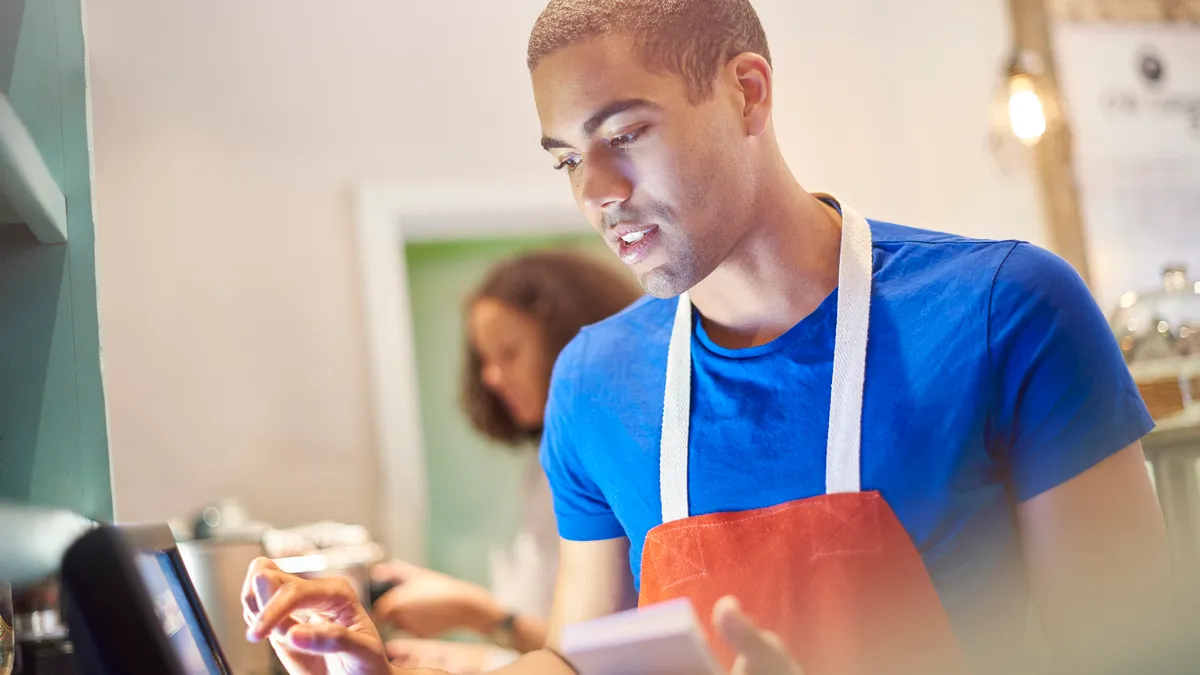 A young coffee shop worker entering the order into the a digital display screen.