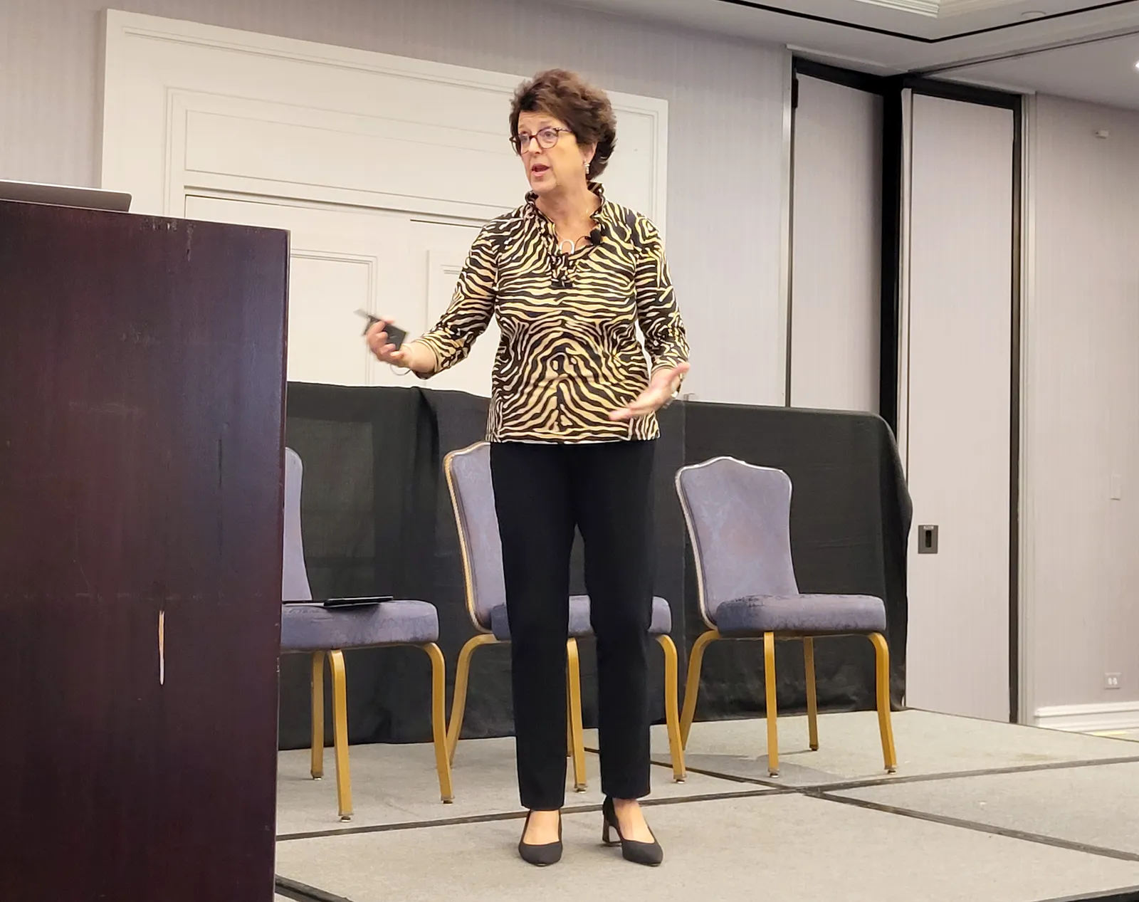 A person stands on a stage addressing an audience while next to a podium.