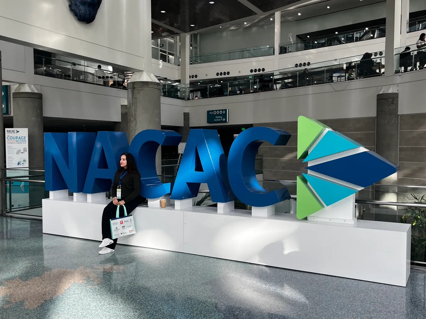 A person posed in front of a large display structure reading "NACAC."