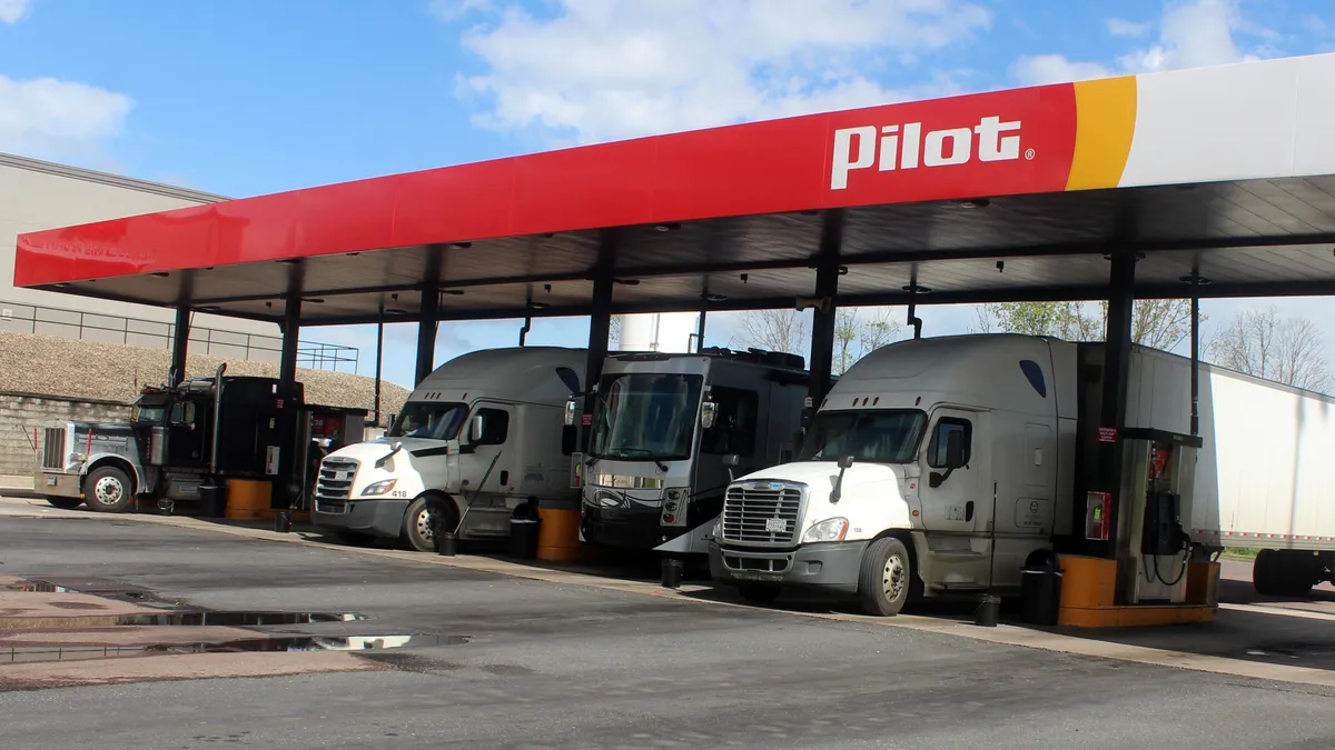 Trucks stop at a fueling area of a Pilot station during a sunny day with blue skies.