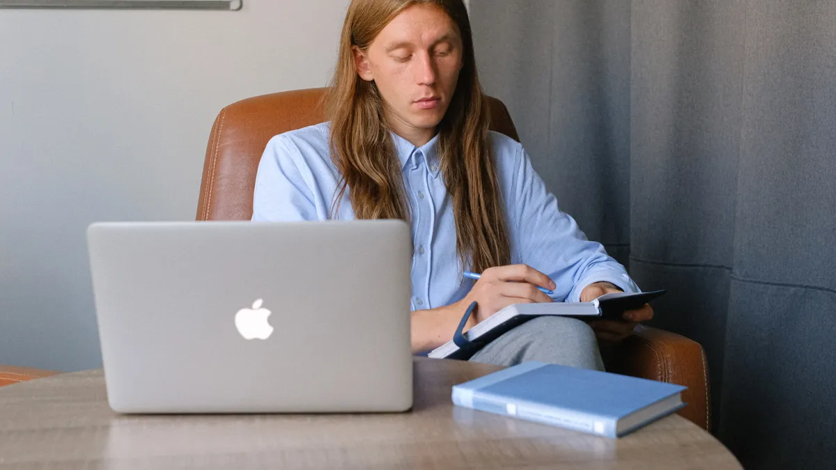 An androgynous person works at their desk with a laptop and notebook