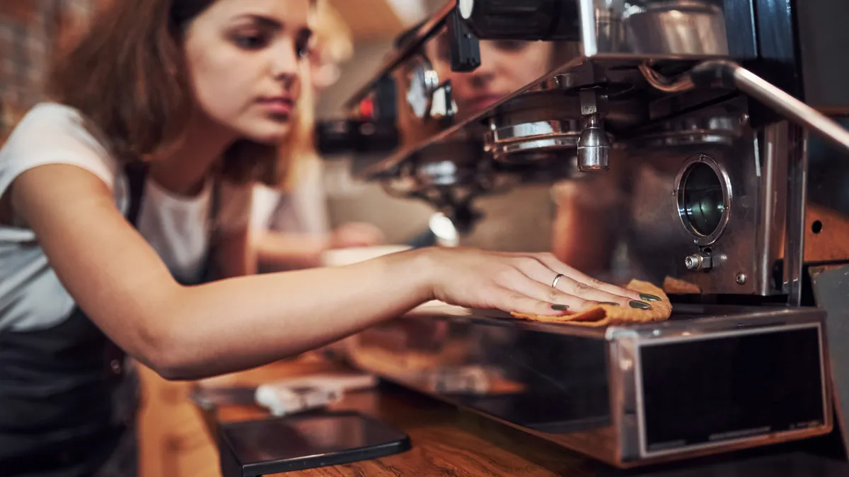 A teenager works at a cafe and cleans an espresso machine,