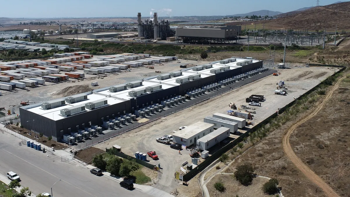 An aerial view of a large industrial building with a power plant and transmission facilities in the background.