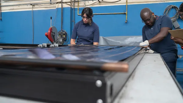 Two people with protective eye glasses and gloves working on a solar panel in a factory.