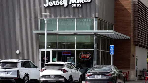 A photograph of a gray building with white signage that says "Since 1956 Jersey Mike's Sub's." There are three cars parked in front of the building.