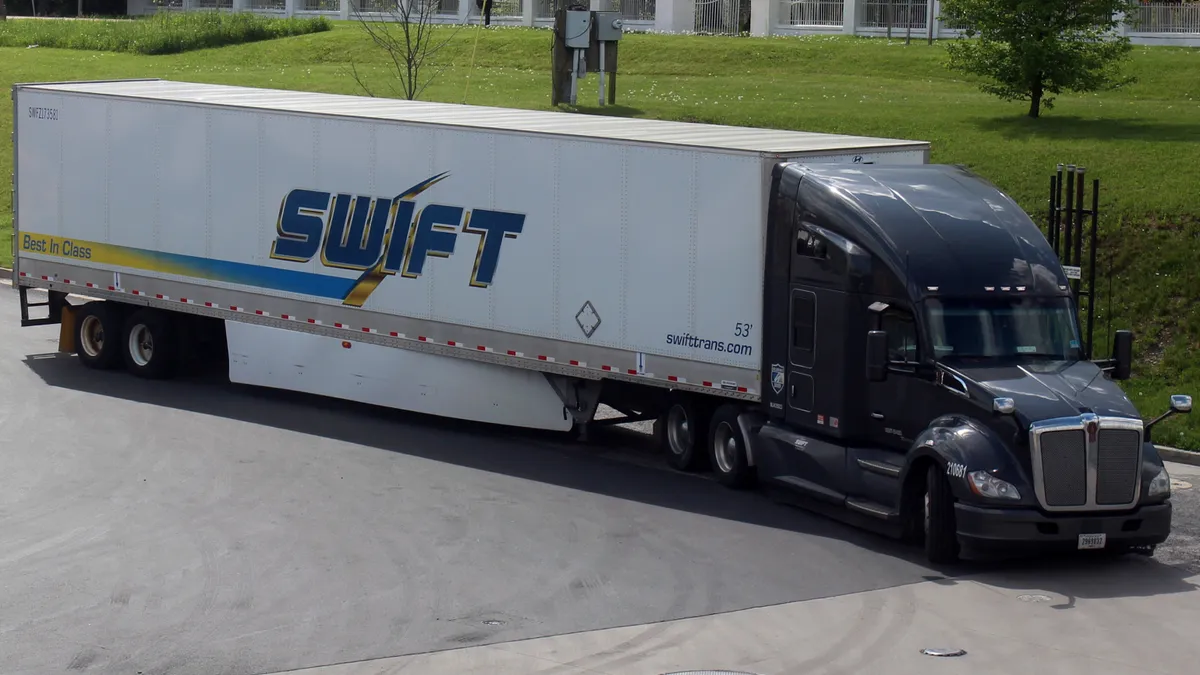 A Swift Transportation tractor-trailer maneuvers in a truck parking lot in Maryland near green grass and blue skies.