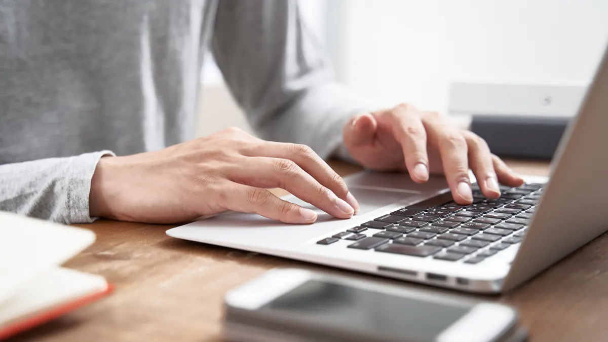 A person in a grey sweater hovers over a laptop with their hands.